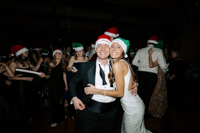 The couple posing for a picture wearing red and green santa hats. 