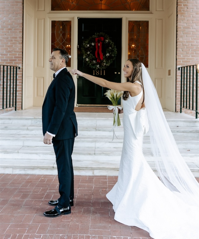 the bride tapping her dad on the shoulder in front of a wreath for a Houston holiday wedding. 
