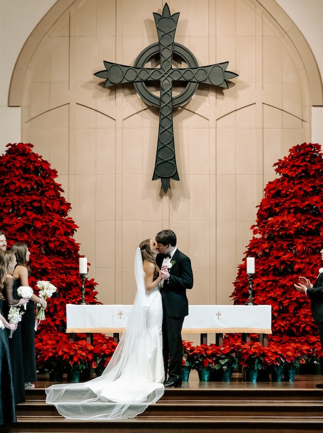 The bride and groom kissing at the altar with large poinsettia trees for a Houston holiday wedding. 