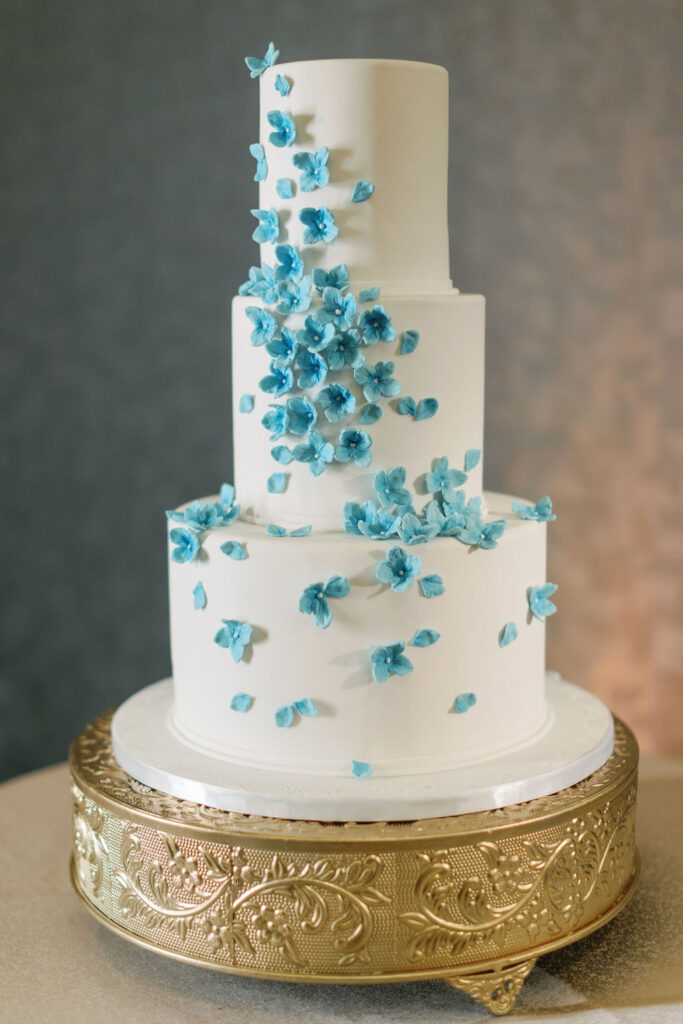 A white three-tier wedding cake with blue fondant florals for blue wedding inspiration.