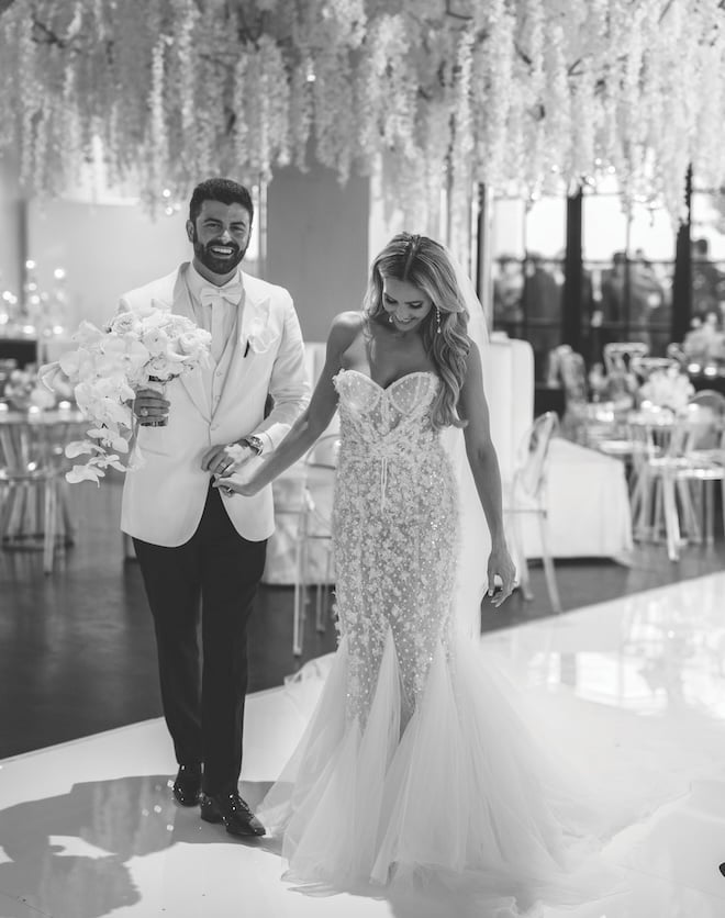 A bride and groom holding hands walking on to the dance floor at Le Tesserae. 