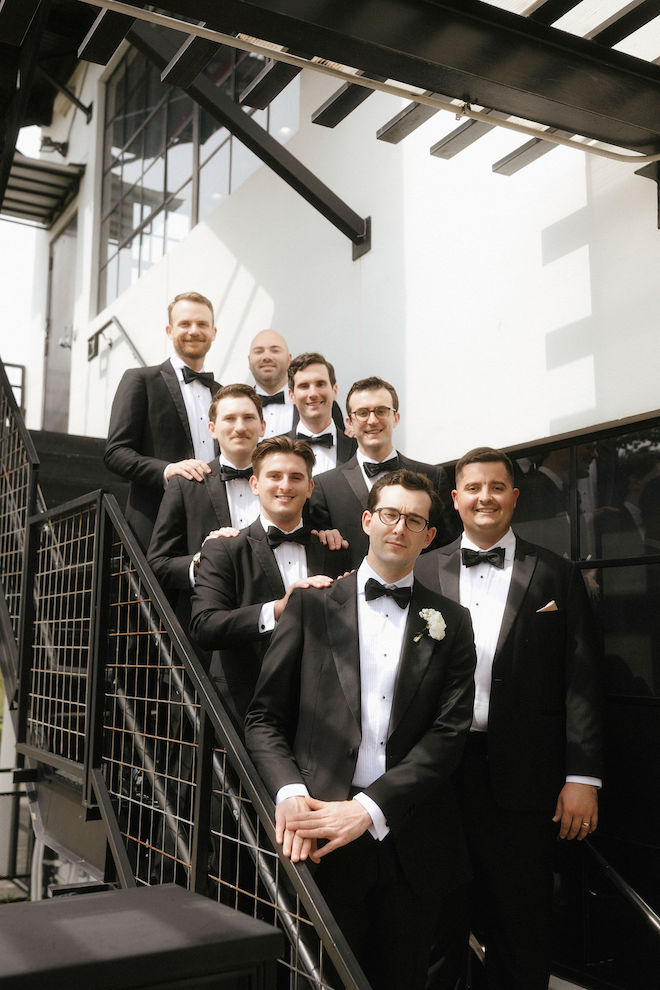 Groom with his groomsmen on outside stairs of venue in tux.