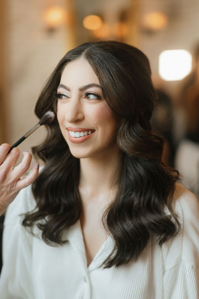 Bride getting her makeup done with a brush touching her cheek.