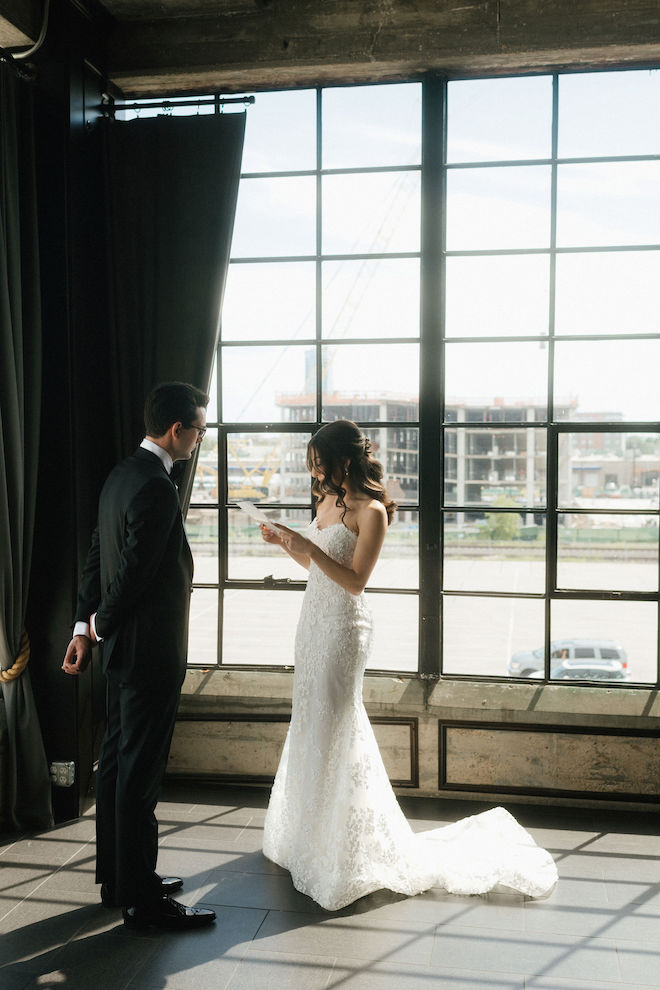 Bride reading her vows to the groom in front big window with light shining in.