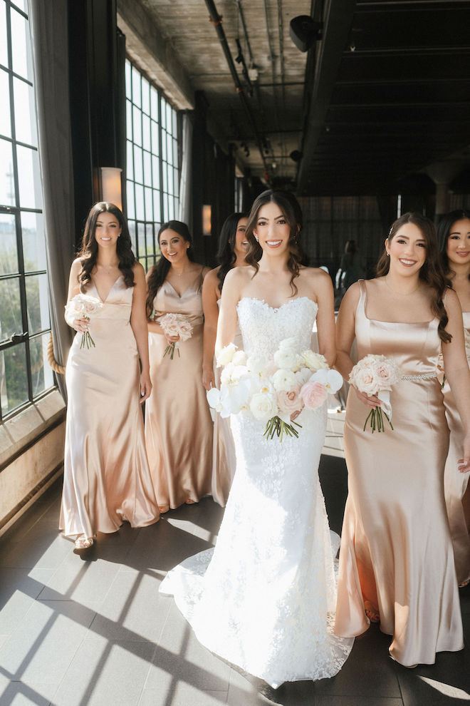 Bride with her bridesmaids in their rose gold dresses and light pink bouquets matching the elegant autumn wedding theme.