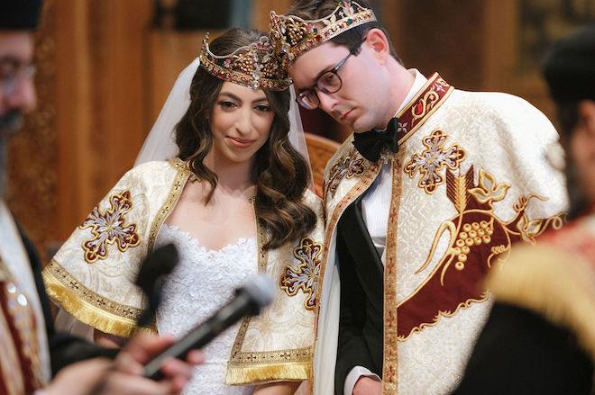 Bride and groom wearing gold crowns and robes during orthodox church ceremony.