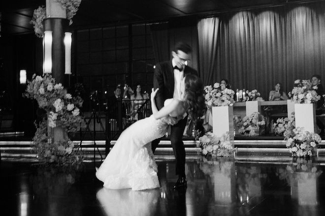 Black and white photo of the groom dipping the bride on the dance floor surrounded by florals in their elegant autumn wedding.