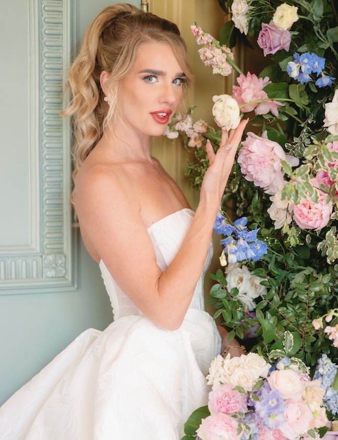 The bride stands next a floral installation in pastel florals. 