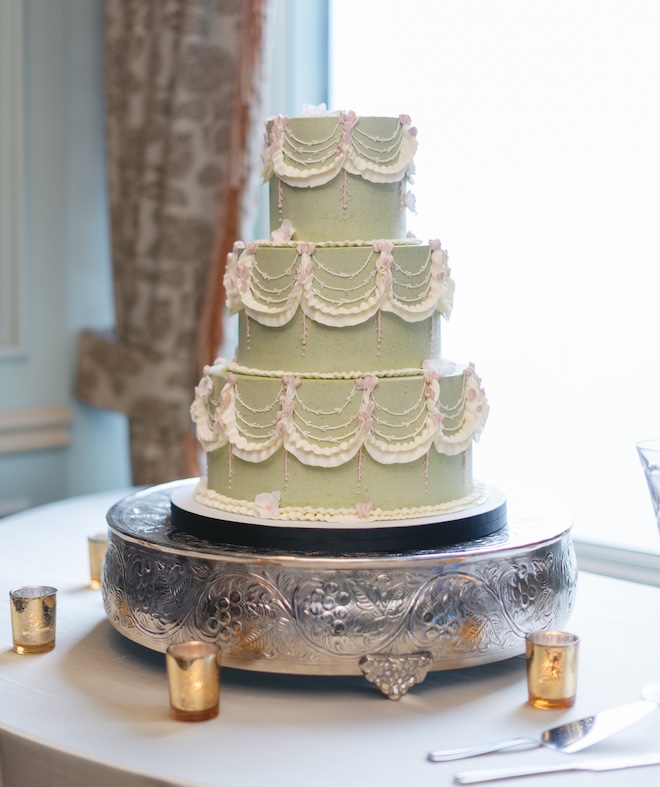 A three-tier green wedding cake with white and pink pipping. 