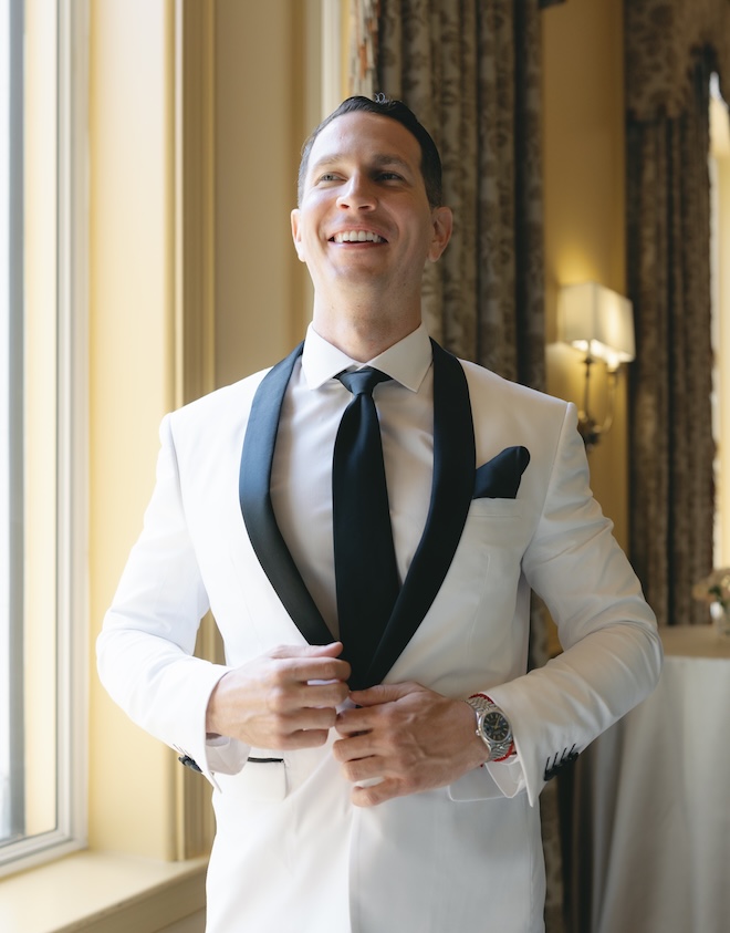 The groom buttons his tuxedo. 