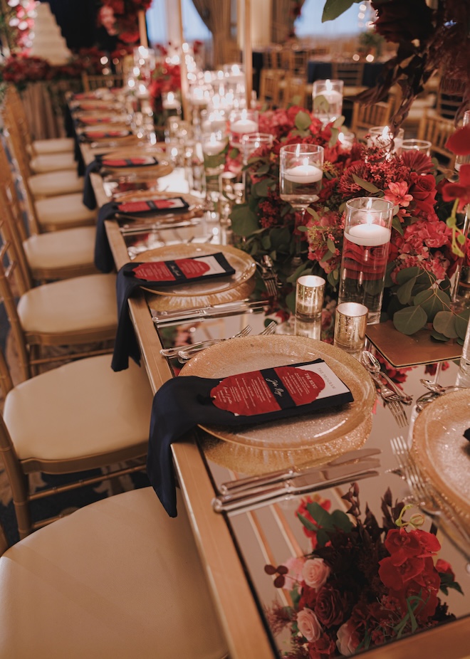 The tablescape decorated with red florals, gold plates and navy linens for a Beauty and the Beast-inspired reception. 
