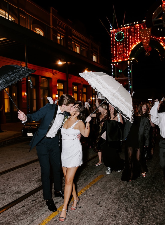 The couple shares a kiss during their second-line exit as wedding guests parade behind them. 