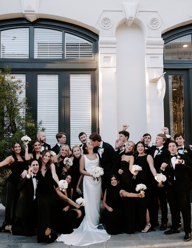 The wedding party celebrates around the bride and groom who share a kiss. 