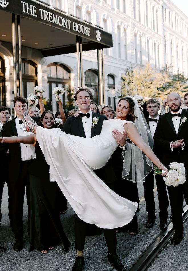 The groom holds his bride as the wedding party cheers behind them. 