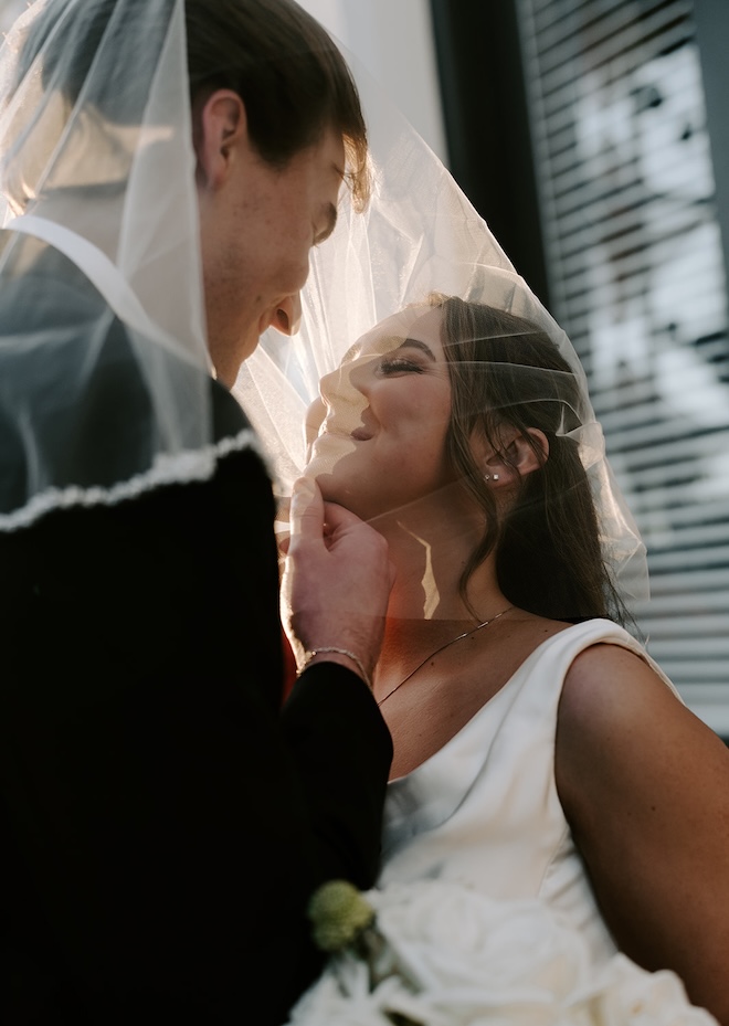 The bride and groom smile under the wedding veil. 