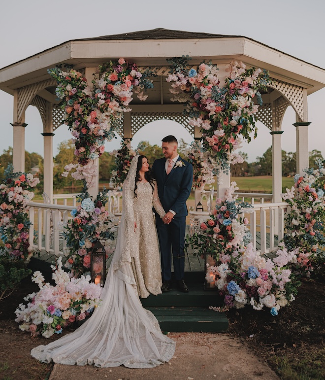 The bride and groom smiling under a gazebo covered in flowers. 