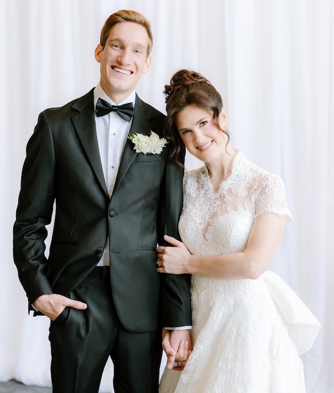 The bride and groom posing for a picture in front of a white backdrop. 