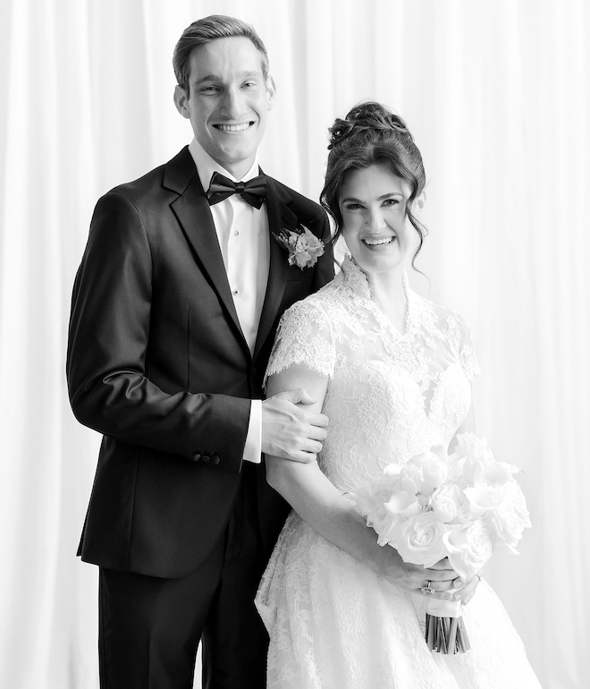 The bride and groom smiling against a white backdrop. 