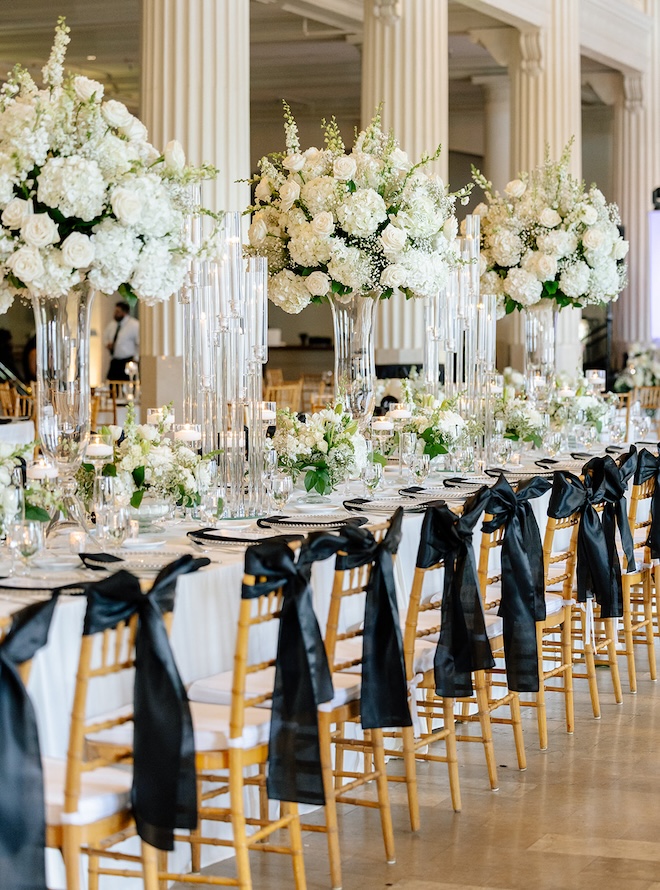 Large white floral arrangements with black bows on the backs of the chairs. 