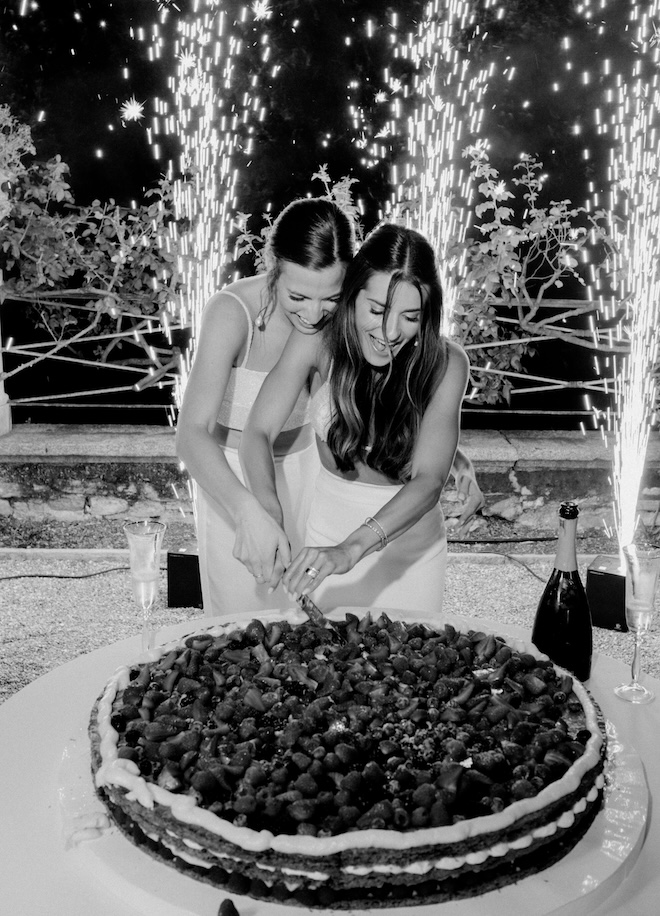 Two brides cutting their cake with sparklers shooting behind them.