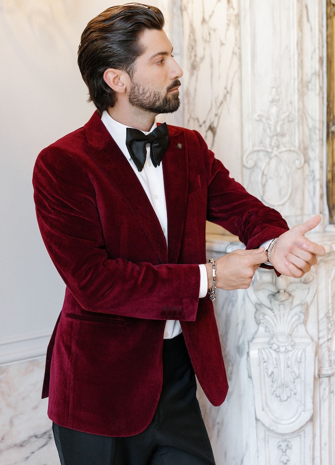 The groom wears a a velvet red suit. 