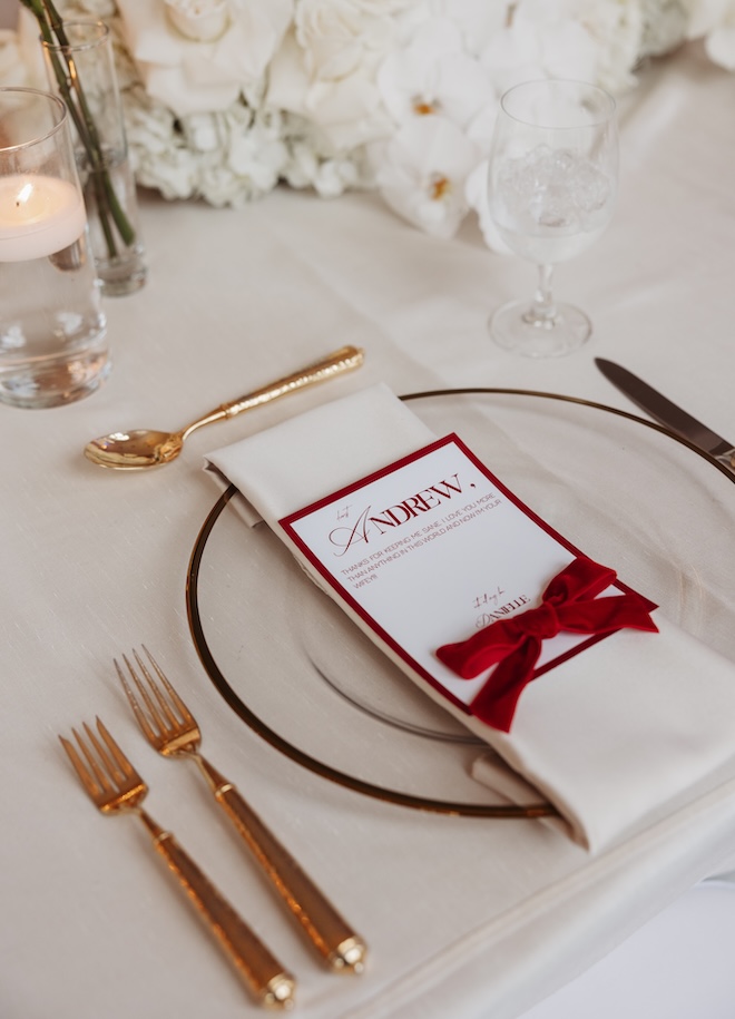 Menus with red font and bows are placed on chargers at the wedding reception. 