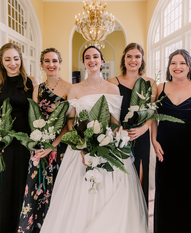 The bride standing with her bridesmaids holding bouquets of palm leaves and white florals. 