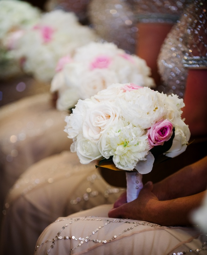 Bridesmaids sitting in a row holding their bouquets of white and pink florals. 