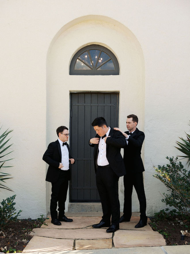 Groomsmen helping groom with jacket getting ready for his dreamy yellow outdoor wedding.