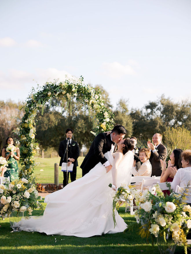 Groom dipping bride down the aisle surrounded by lush florals in their dreamy yellow outdoor wedding.