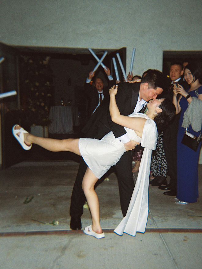 Groom dipping the bride in grand exit surrounded by cheering guests.
