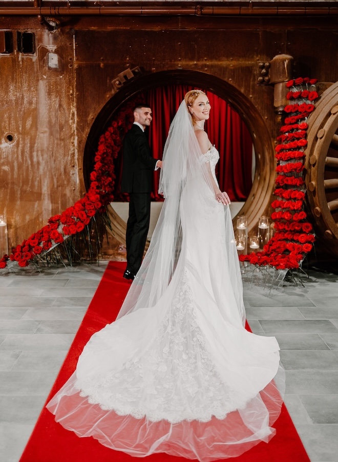 The bride and groom hold hands as they walk into The Vault at Corinthian Houston decorated in red roses.