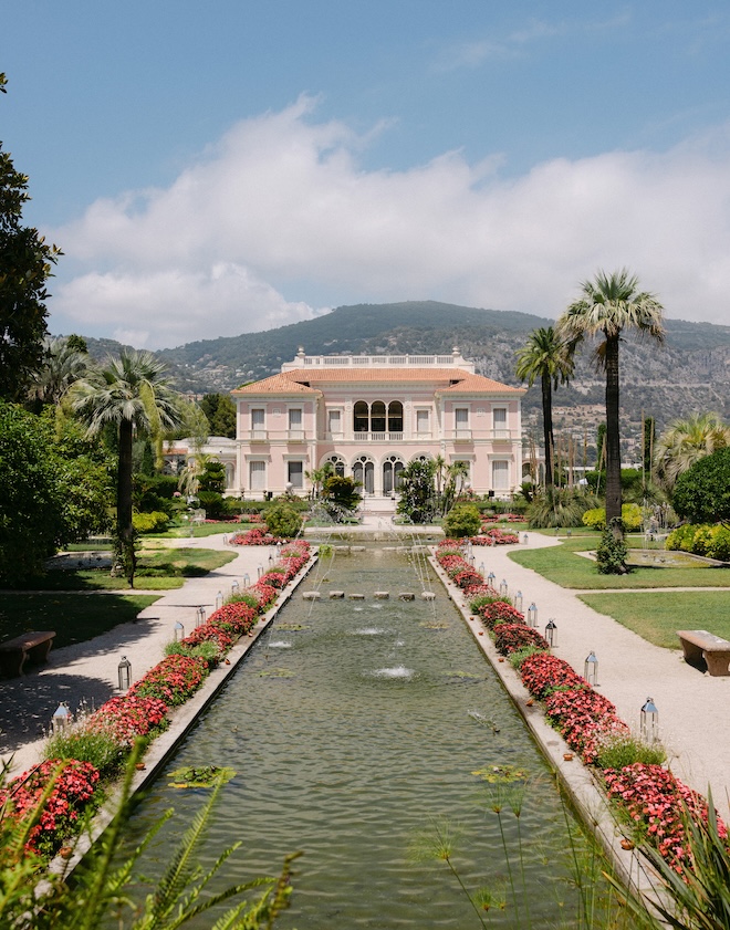 A pond and waterfall is at the front of historic pink palace on the French Riviera.