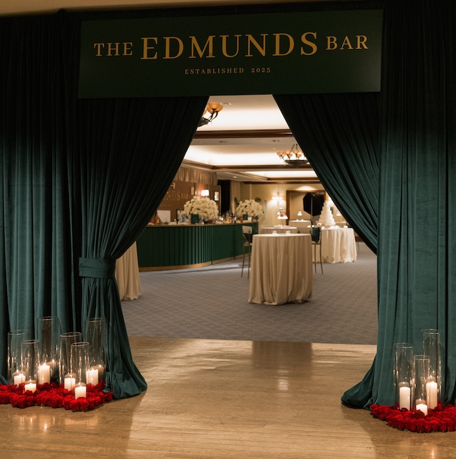 Green curtains and a sign that says "The Edmunds Bar" leading into a room with cocktail tables and their wedding cake. 