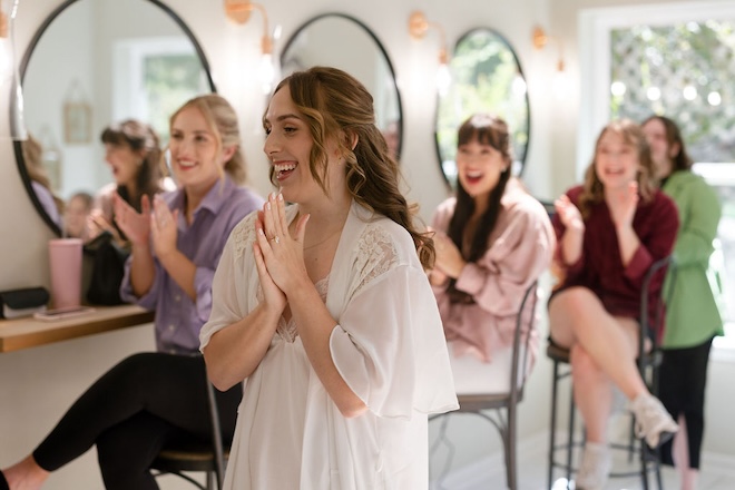 A bride and her bridesmaids getting ready and clapping.