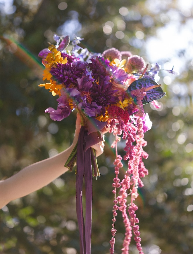 A bouquet by Fashionable Florist consisting of jewel-toned flowers of purple. pink, blue and yellow. 