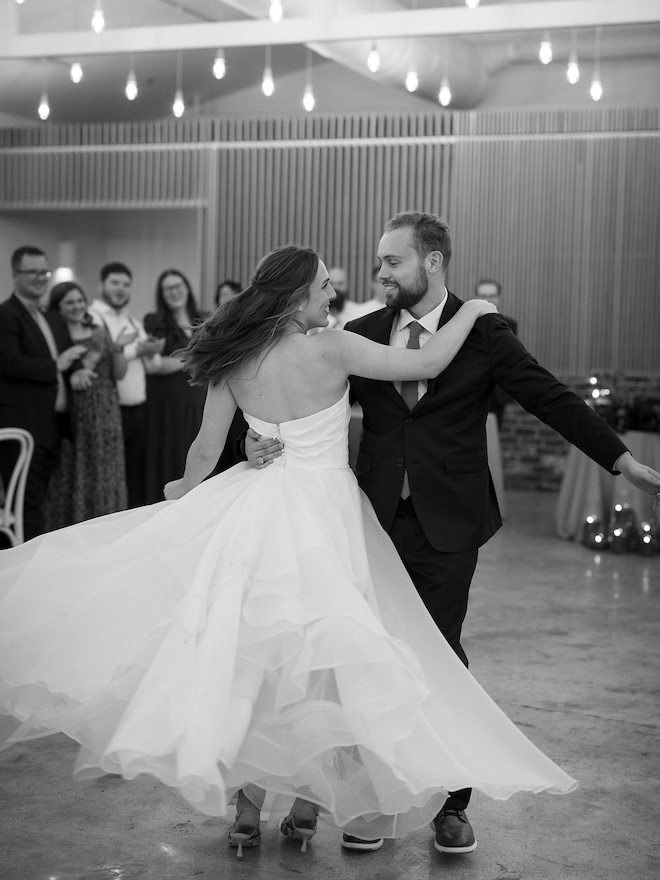 The bride and groom dancing their first dance with guests clapping behind them. 