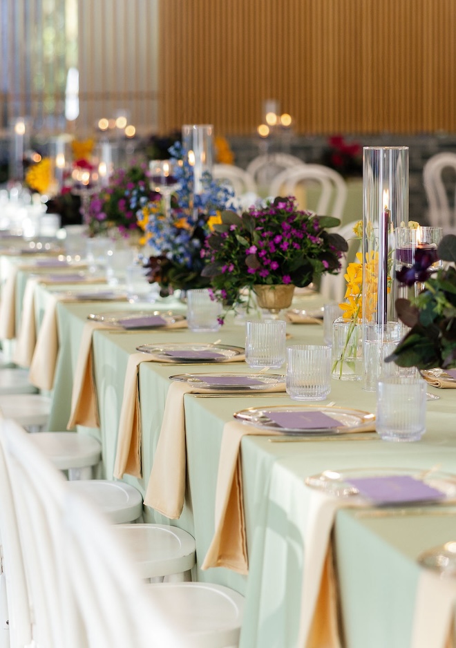 The reception table decorated with candles and bud vases filled with jewel-toned florals. 