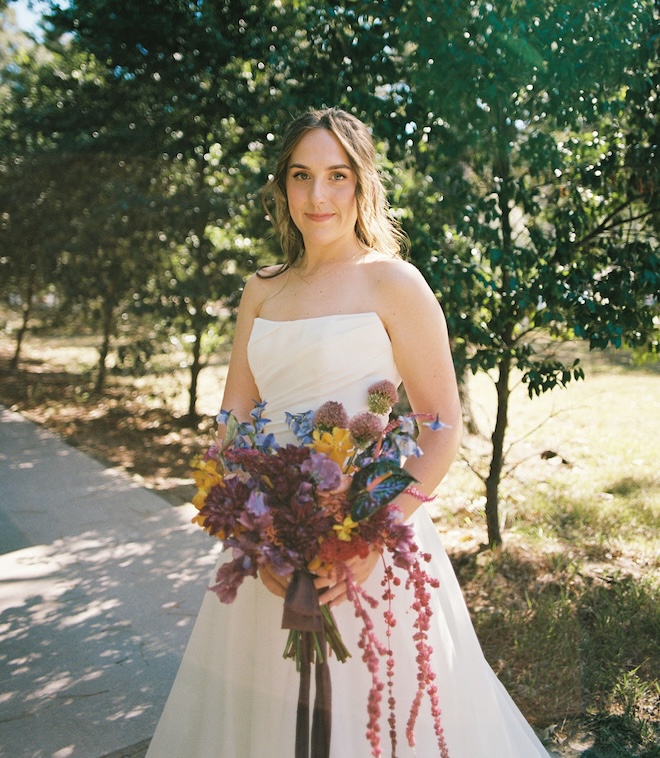 The bride smiling holding her boquet of jewel-toned florals. 