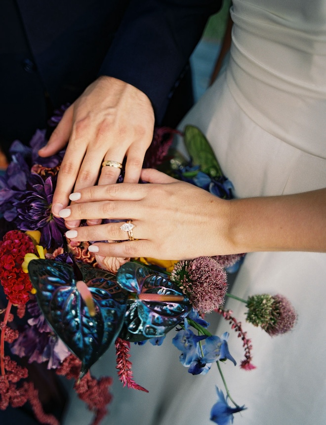 The bride and groom showing off their rings against the bride's bouquet. 