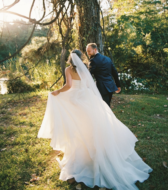 The bride and groom smiling at each other and running next to a large tree. 