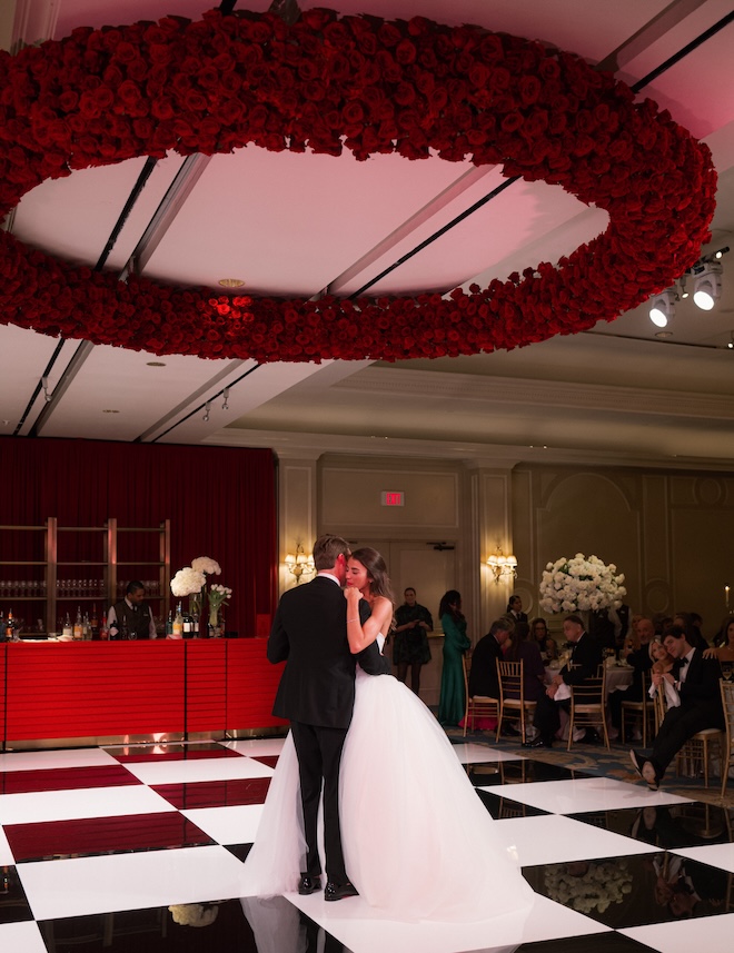 The bride and groom dancing on a black and white checkered dance floor with a rose floral arrangement above them. 