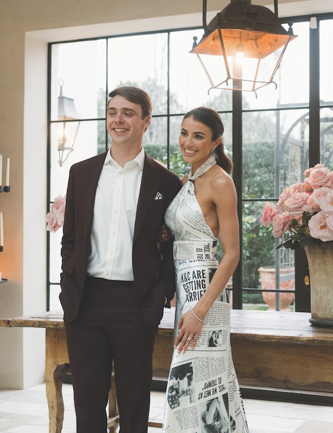 The bride smiling for a photo with the groom while wearing a custom newspaper gown for her rehearsal dinner. 