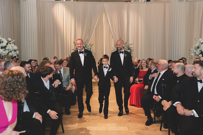 The grooms' son walks them both down the aisle at their wedding ceremony in Corinthian Houston.