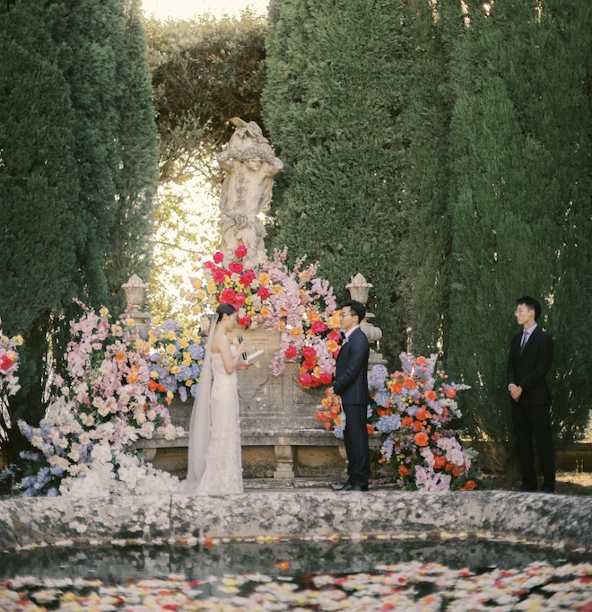 The bride reading her vows to the groom at their colorful garden wedding in Tuscany. 