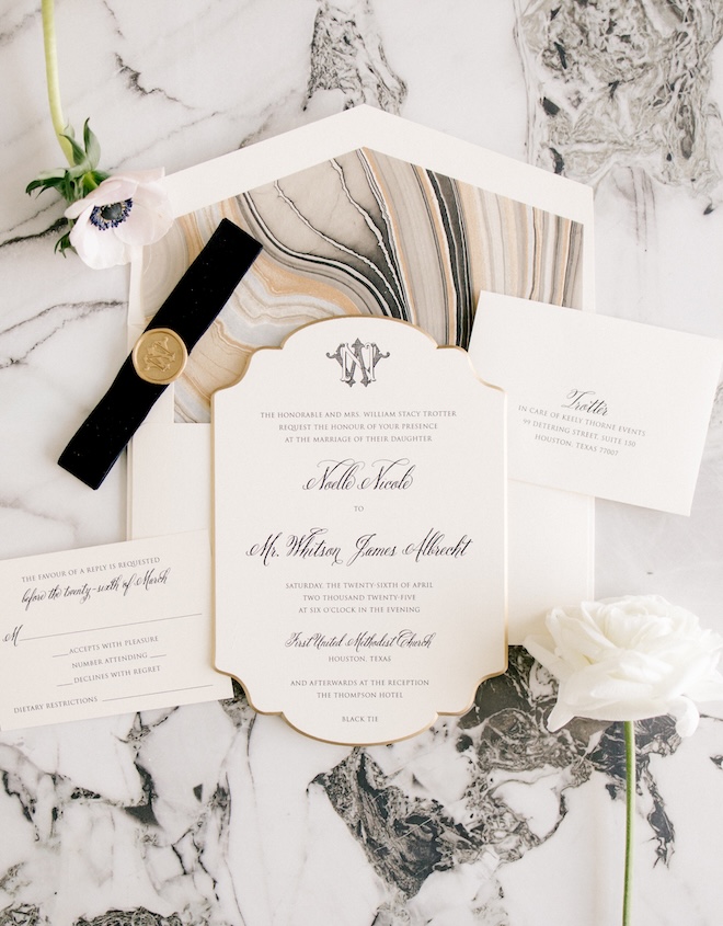 Black, gold and metallic wedding stationery and invitations sit on top of black and white marble counters. 