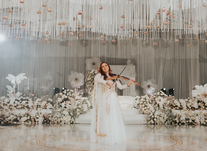 An electric violinist plays at the wedding reception surrounded by pastel florals. 