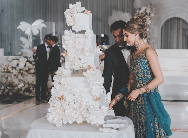 The couple cut into their white wedding cake embossed with flowers. 