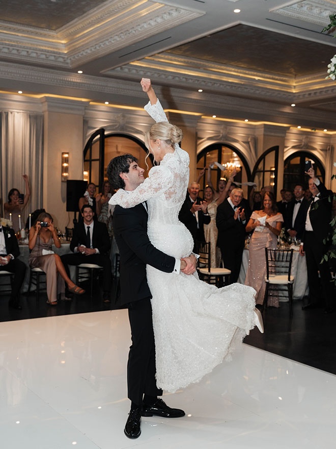 The groom picks up the bride on the dance floor as guests cheer. 
