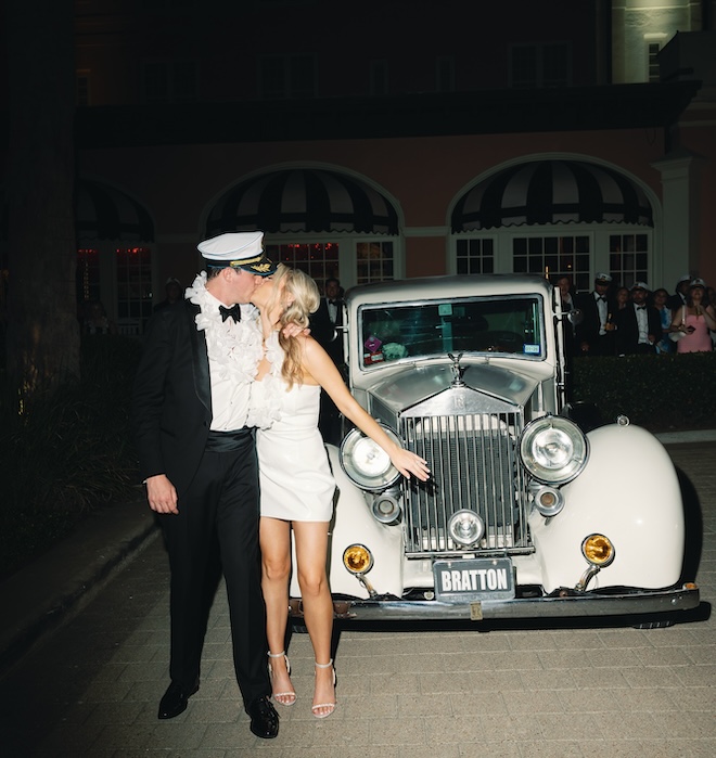 Bride and groom kissing in front of vintage getaway car.